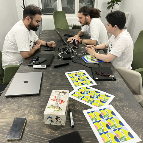 Three colleagues working across a meeting table covered in laptops and printed card sheets